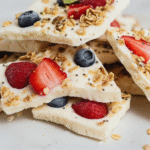 Stack of yogurt bark shards with berry swirls on plate, slate-gray linen