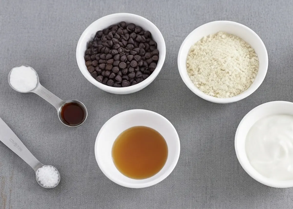 dairy-free protein yogurt bark ingredients: coconut yogurt, plant protein powder, almond butter or oil, maple syrup, cacao nibs, mini chocolate chips, salt, sheet pan with parchment