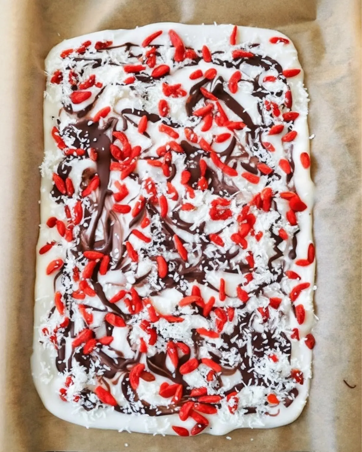 coconut yogurt bark on parchment with goji berries, shredded coconut and dark-chocolate swirls
